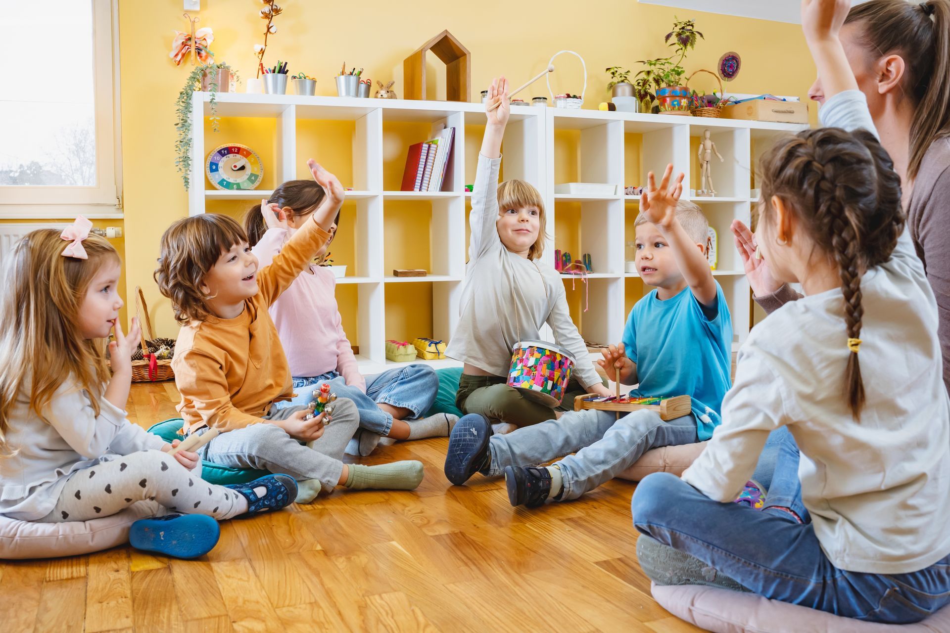 A group of children are sitting on the floor with their hands in the air.