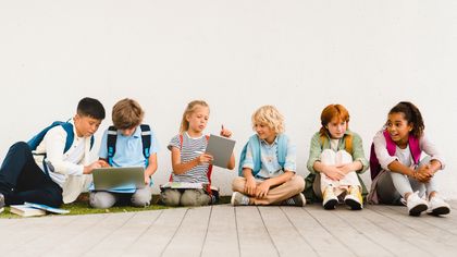 A group of children are sitting on the floor using laptops and tablets.