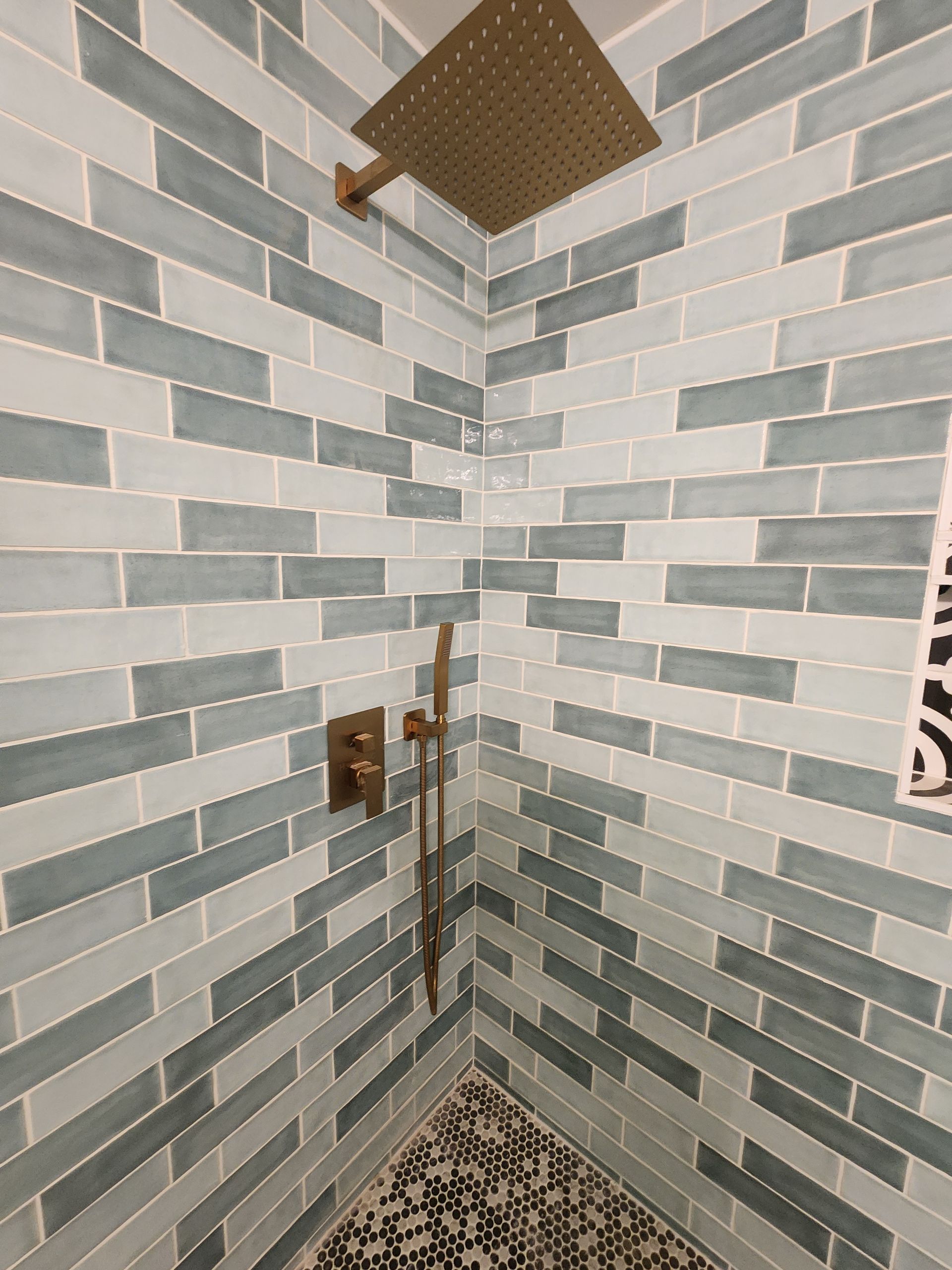 Shower with blue and white tile, gold fixtures, and black and gray floor tiles.