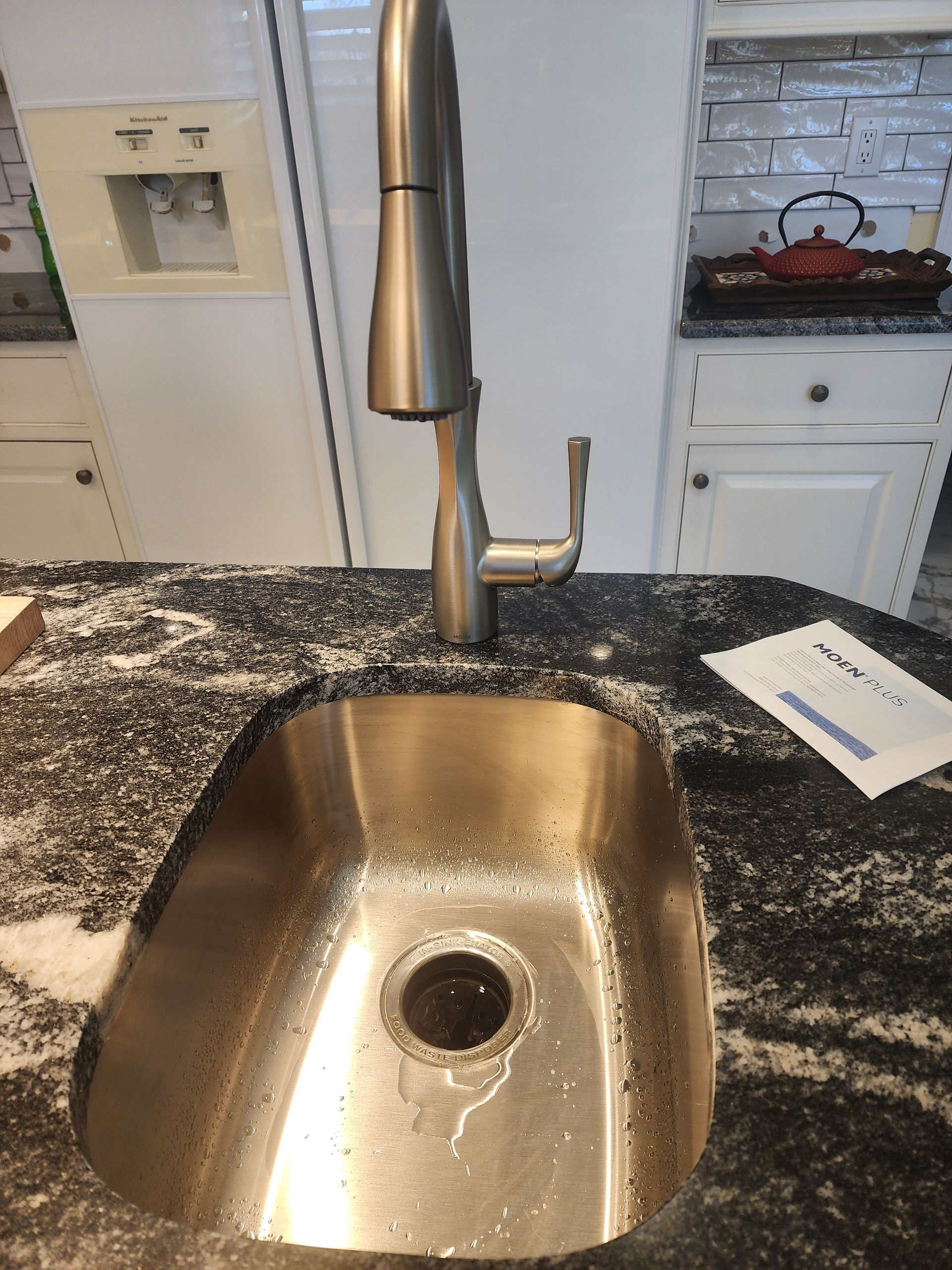 Stainless steel kitchen sink with faucet, set in black granite countertop.