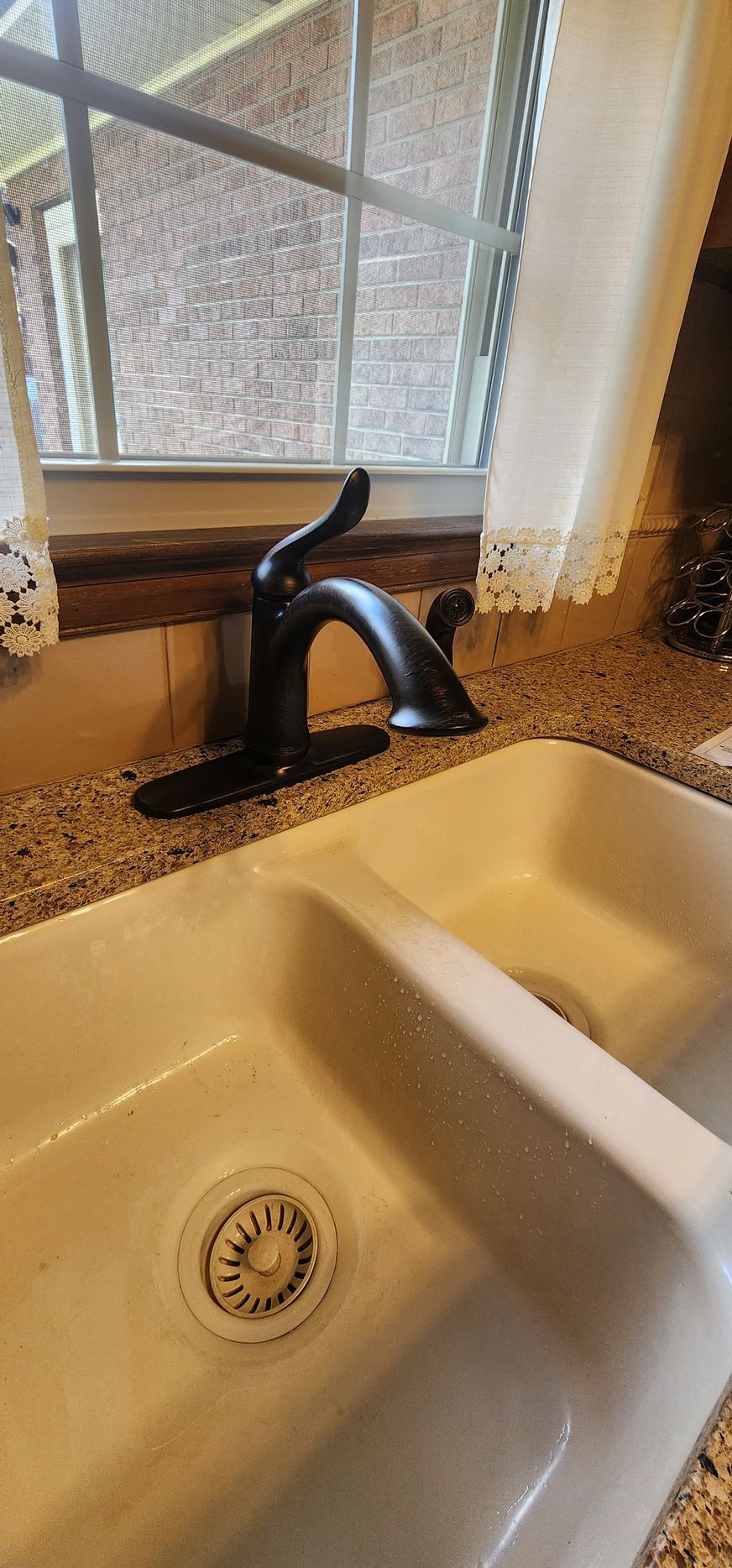 A black faucet sits on a speckled countertop above a white, double sink. A window is behind it.