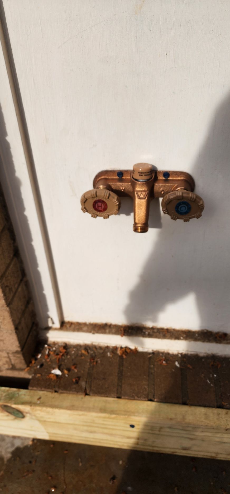 Copper faucet with red and blue handles mounted on a white wall.