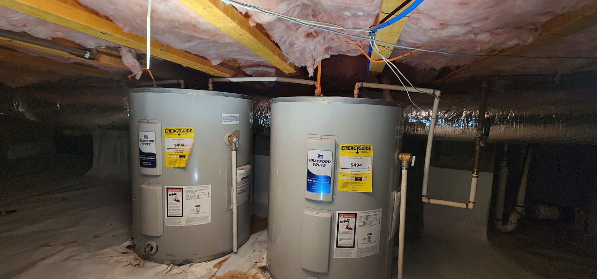 Two cylindrical water heaters in a crawl space, with exposed insulation and ductwork.