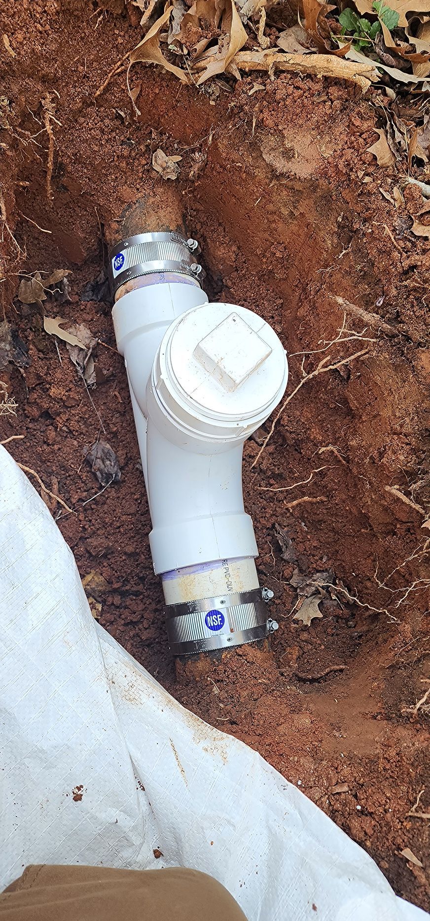 White PVC pipe with cap and connectors buried in red dirt. A white cloth is visible on the side.