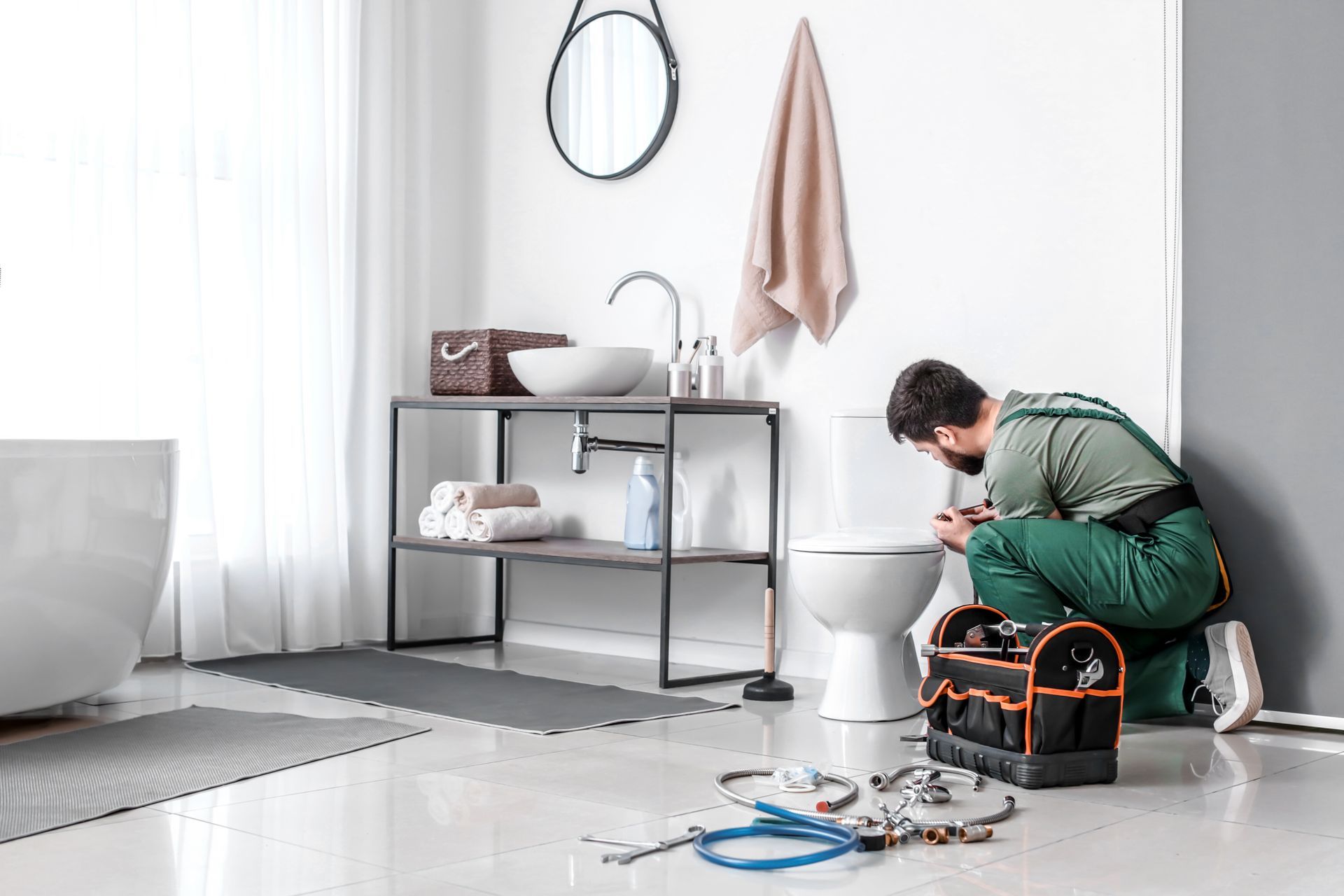 plumbing renovations near me Plumber kneeling by a toilet in a bright bathroom, tools in a bag nearby.