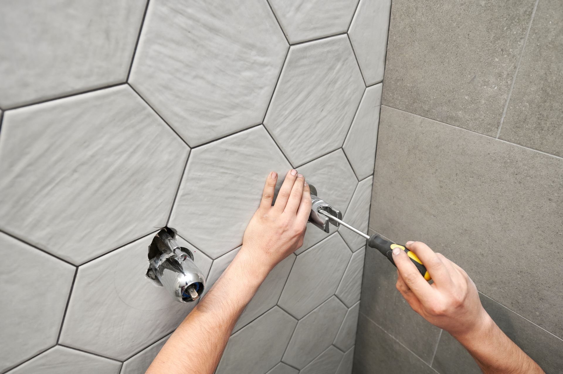 plumbing services in cleveland nc Person using a screwdriver to install plumbing fixtures on a tiled shower wall.