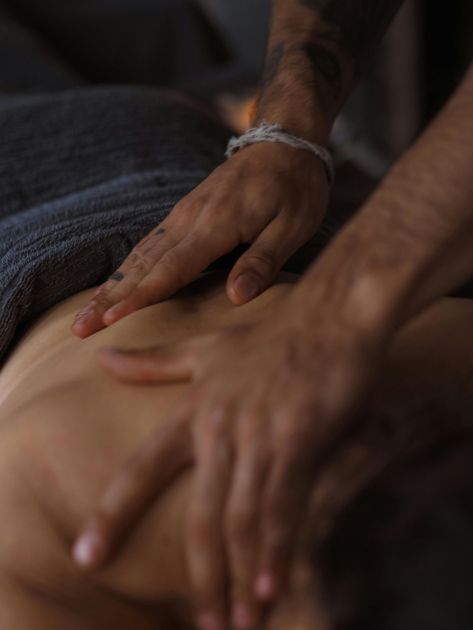 Hands giving a back massage on a person’s bare back in dim light