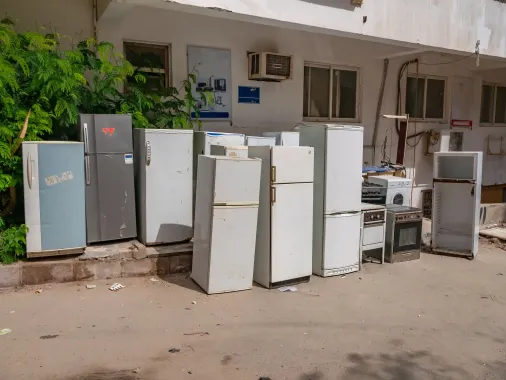 Pile of old refrigerators and appliances against a building, outside.