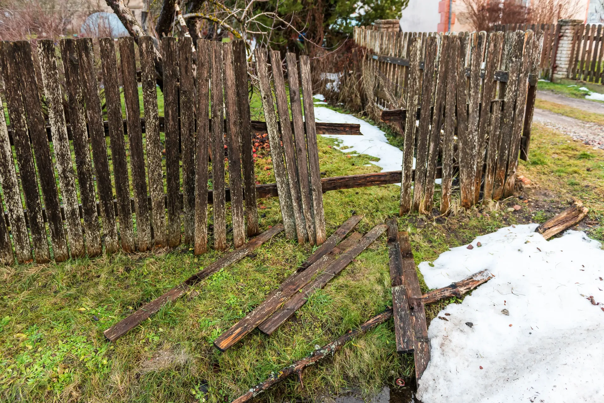 Broken wooden fence by a muddy path with patches of snow on the ground