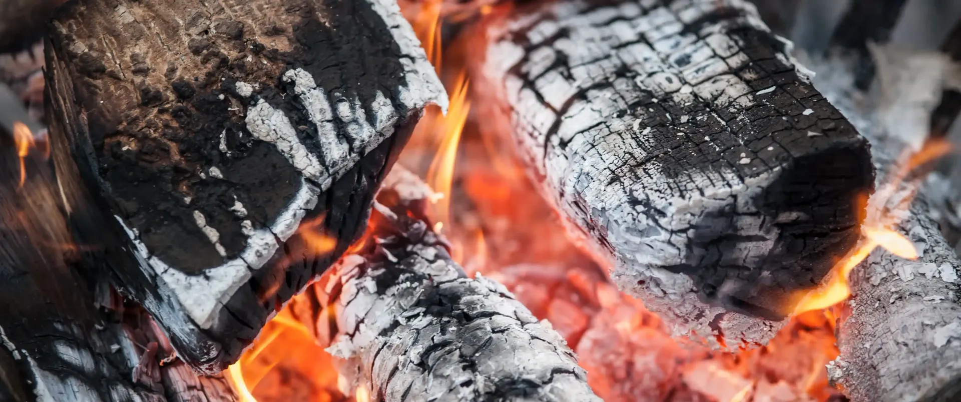 Close-up of glowing embers and charred logs with orange flames