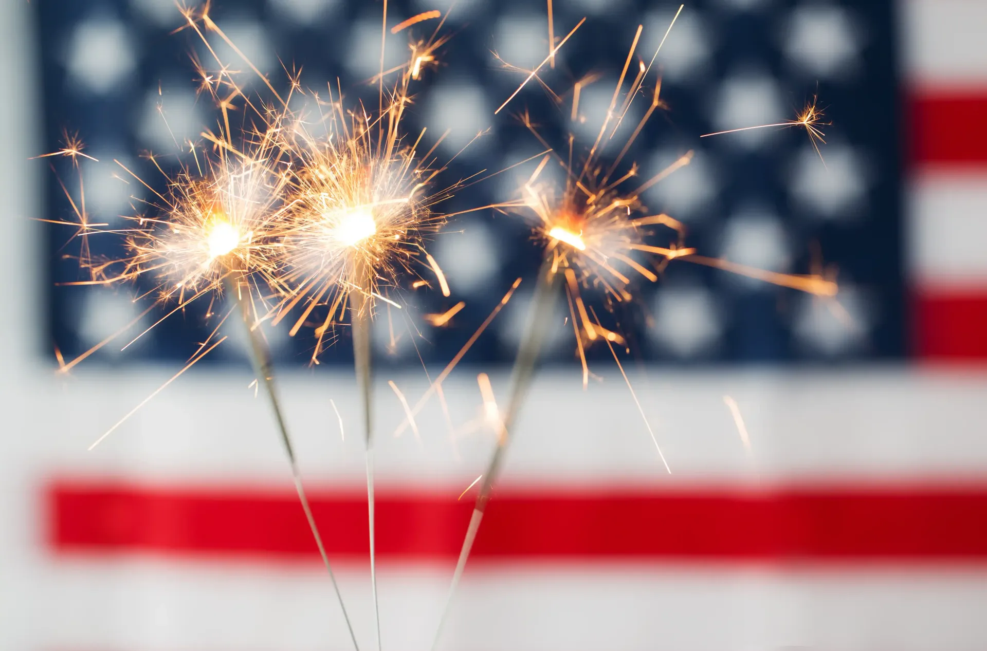 Sparklers sparkling in front of a blurred American flag background