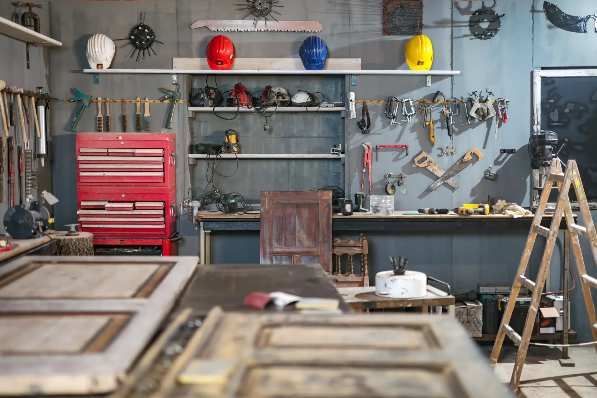 Garage with red tool chest, shelves, hard hats, ladder, and tools scattered around.