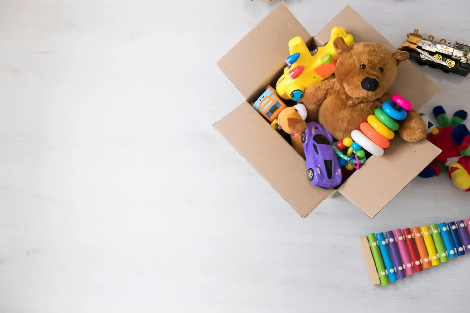Cardboard box filled with colorful toys and a teddy bear on a white background