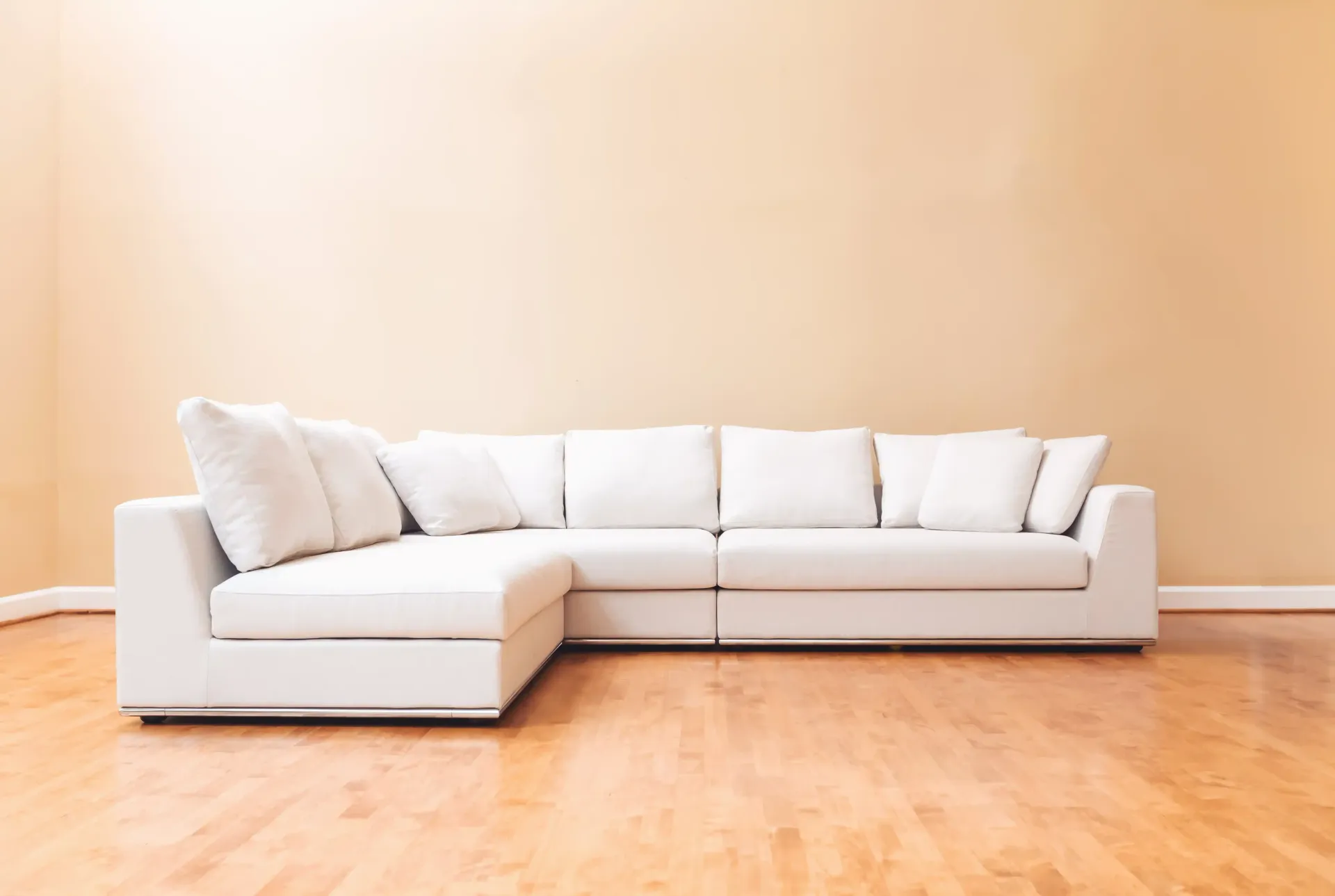 White sectional sofa in a bright, empty living room with light wood floor and beige walls