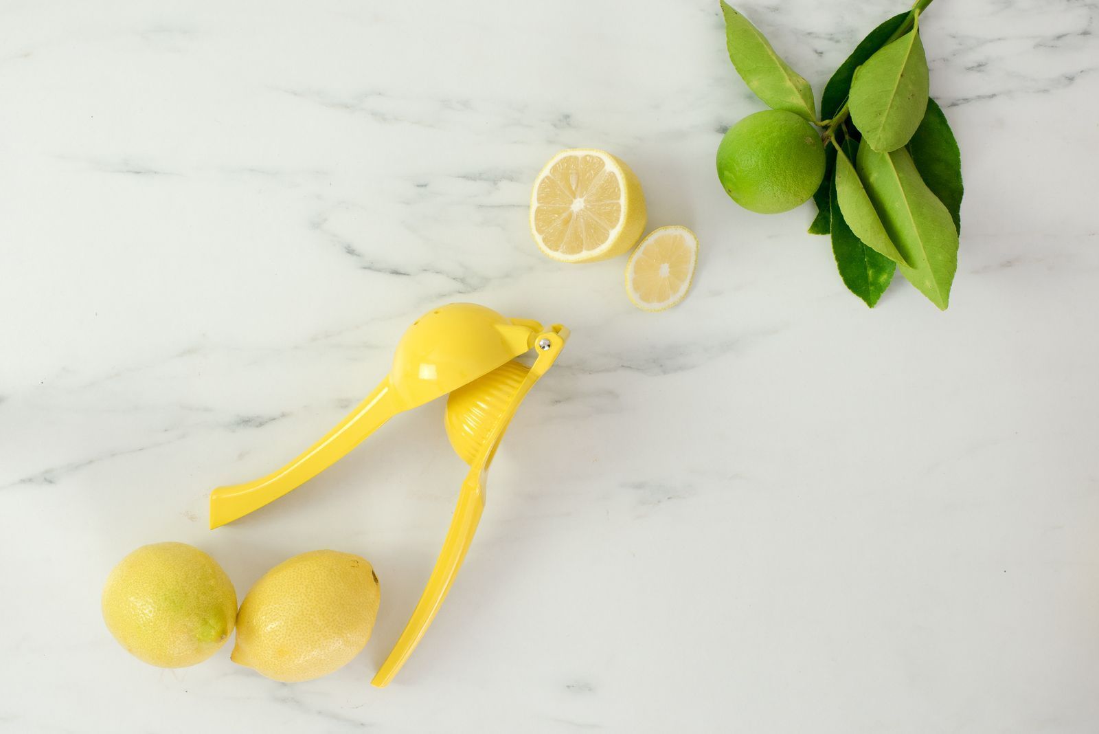 Yellow lemon squeezer with lemons and lemon slices on a white marble surface
