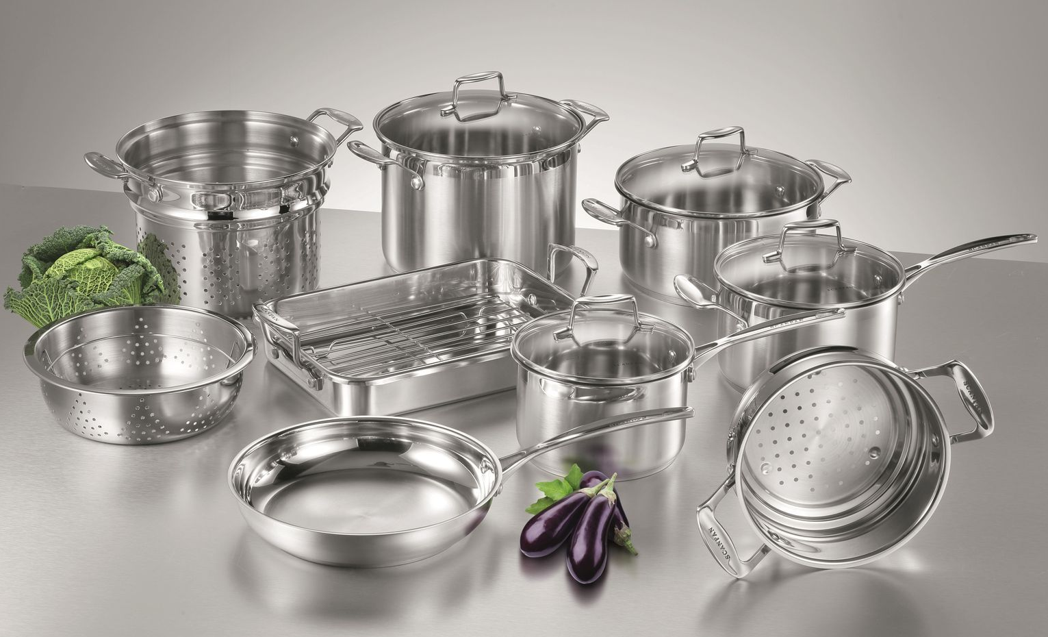 Assorted stainless steel cookware set on a white background, including pots, pans, colander, and utensils