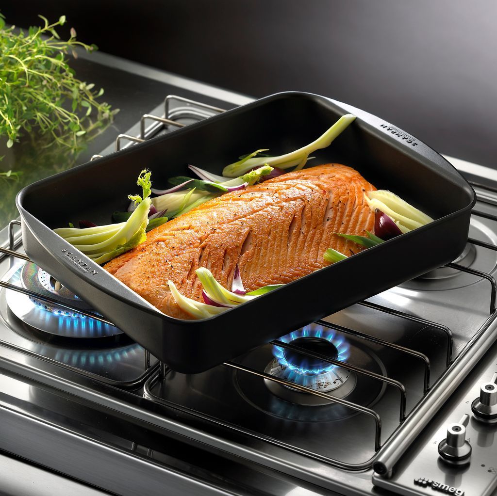 Salmon fillet roasting in a black pan on a gas stovetop with green vegetables