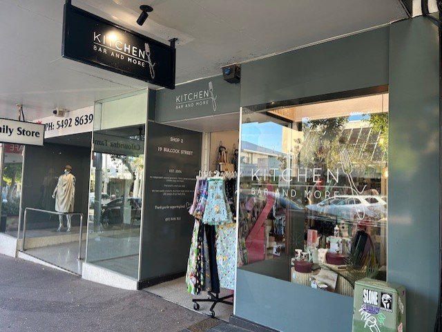 Storefront of a boutique with clothing racks and dresses displayed under a covered sidewalk.