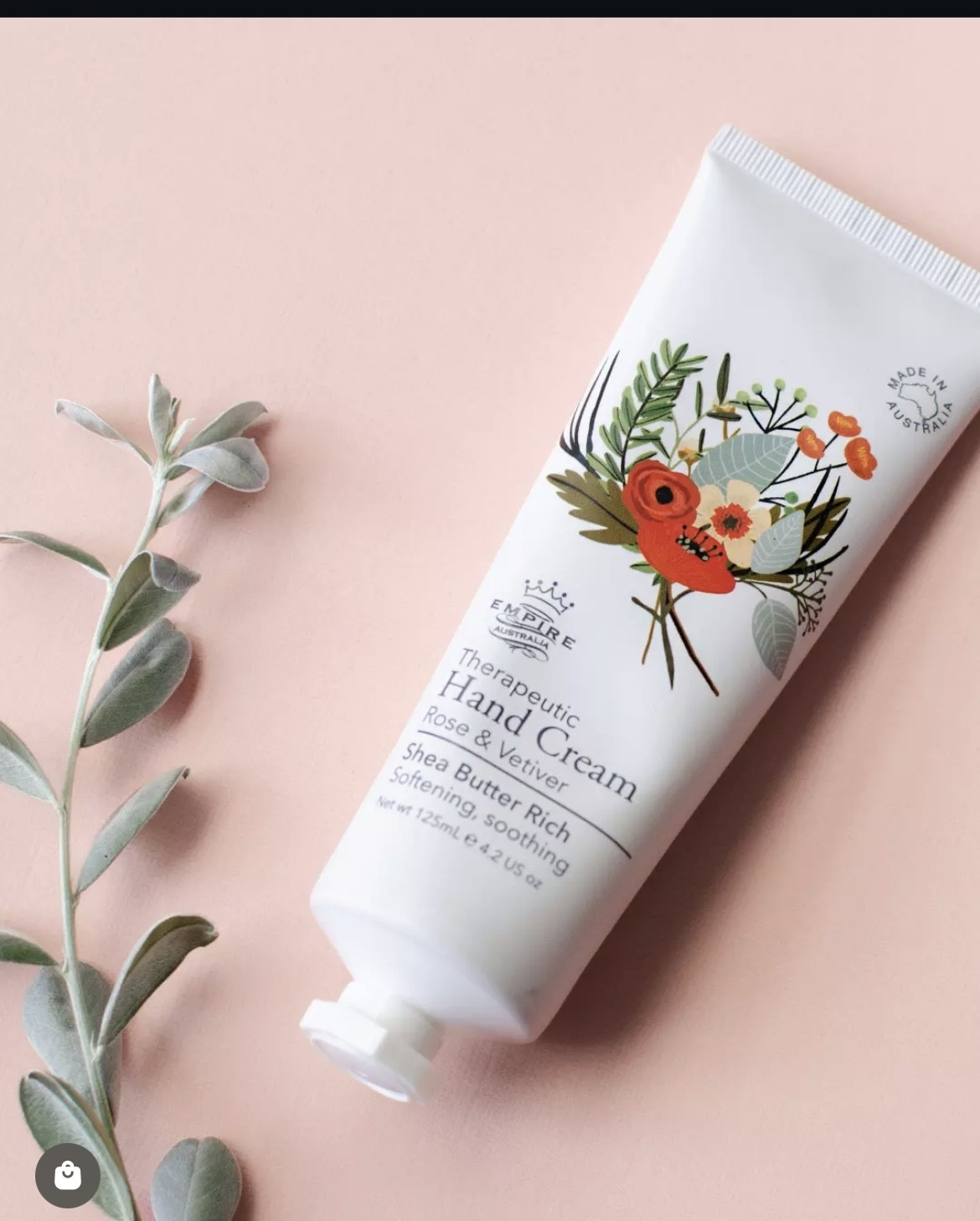 White floral hand cream tube on a blush pink background with a small eucalyptus sprig