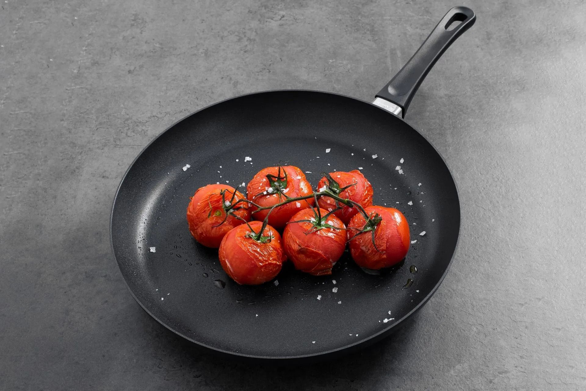 A Black Pan Sits on a Gray Surface, Containing a Cluster of Roasted Red Tomatoes — Kitchen Bar and More In Caloundra, QLD