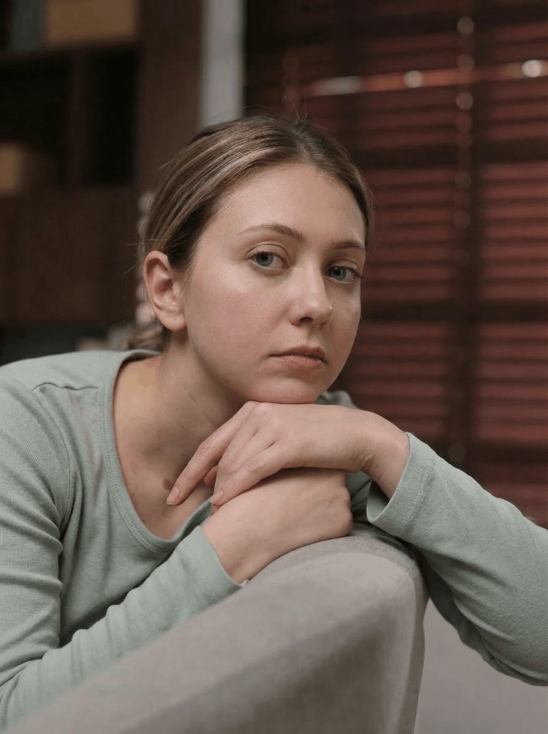 Woman with blonde hair, leaning on a sofa, looking somber with a concerned expression.