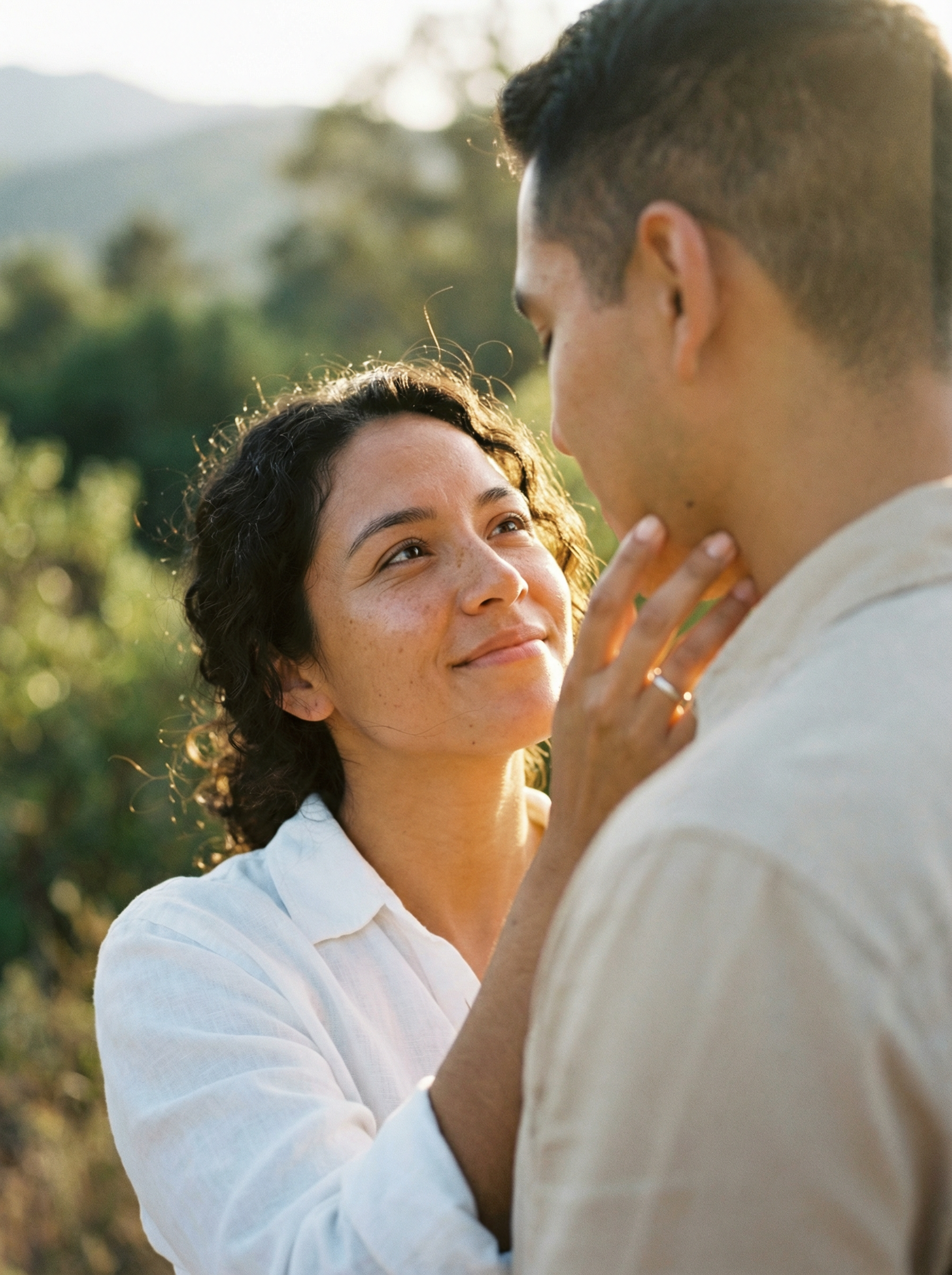 Woman with dark curly hair looks lovingly at a man in white shirt, outdoors.