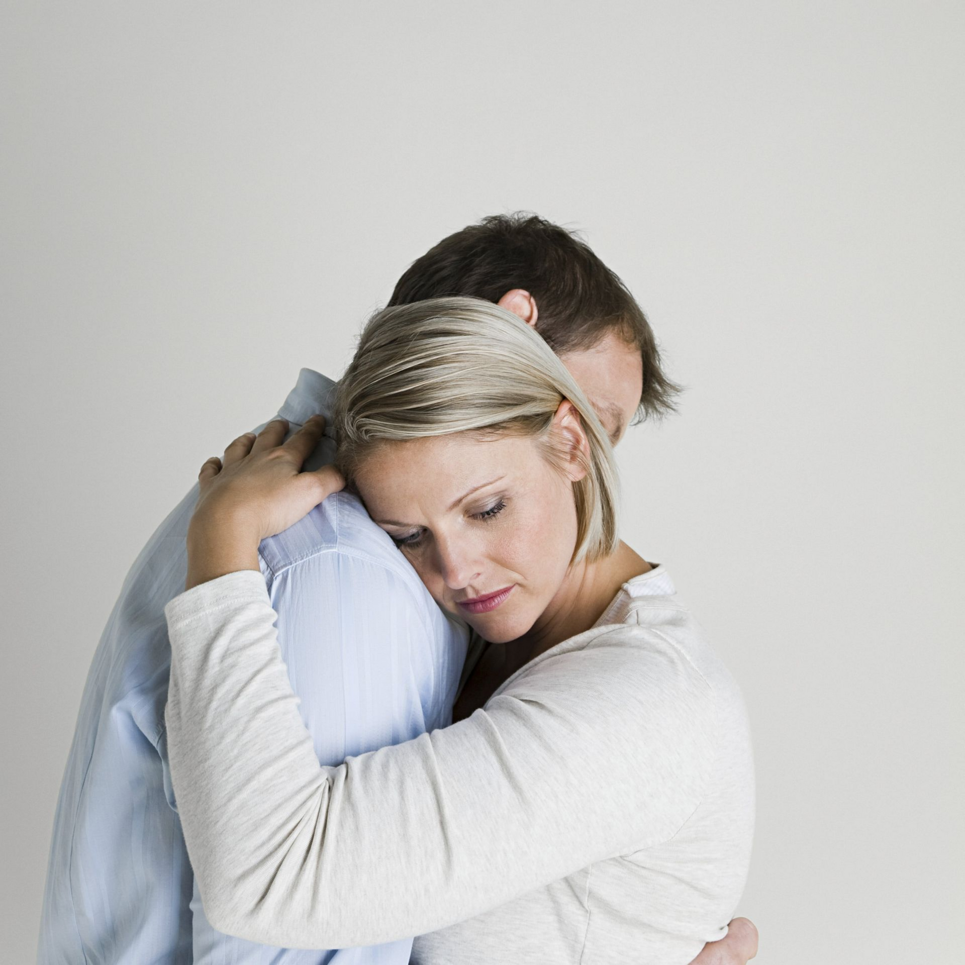 Woman hugs a person with their head on the woman’s shoulder. Both have somber expressions.