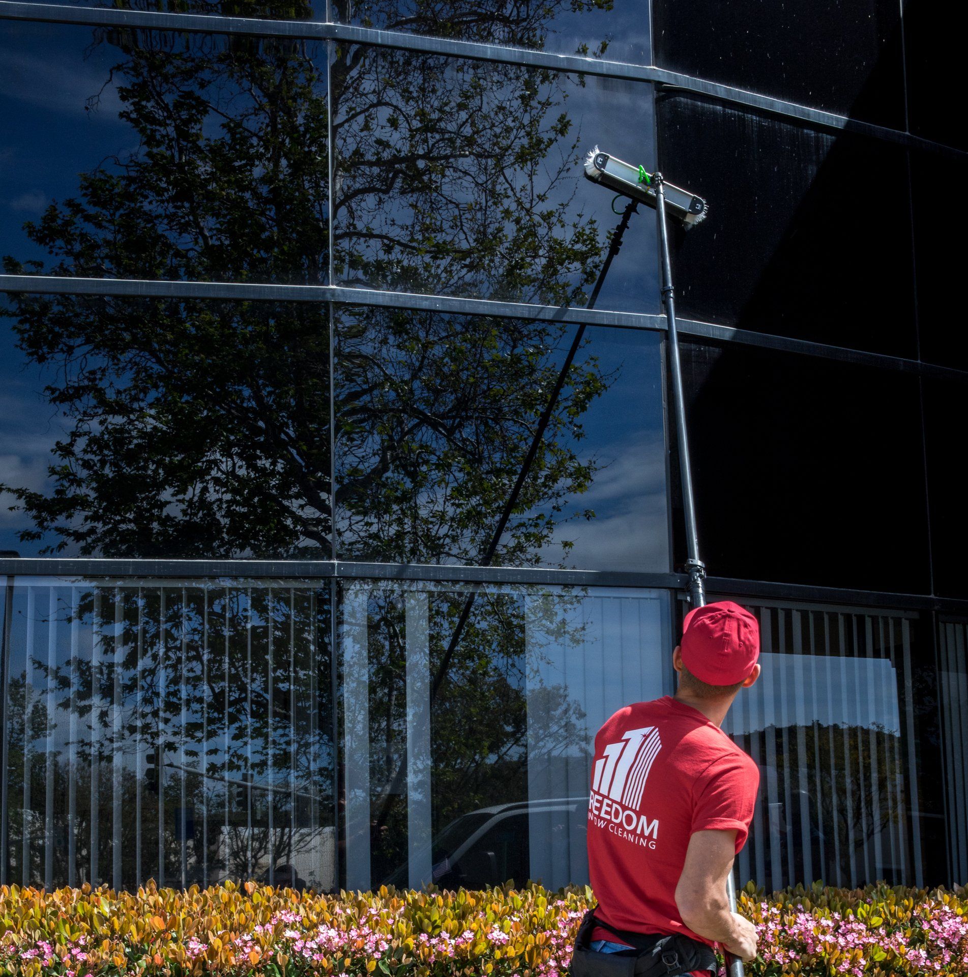 Person in red shirt using a long pole to clean a modern glass building facade