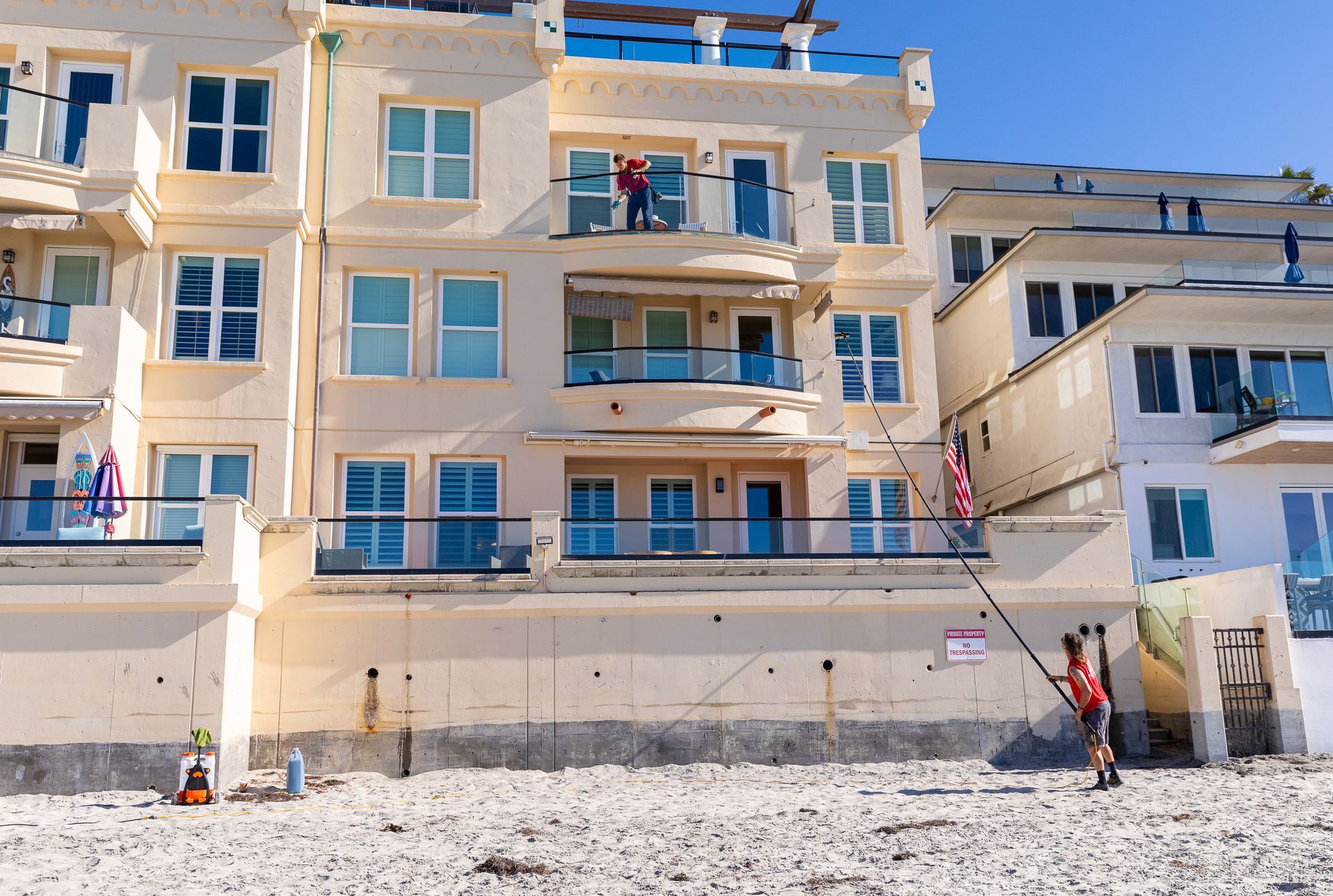 Pastel apartment building with balconies beside a sandy beach, with a few people outside