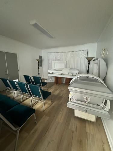 Funeral home interior with two caskets, chairs, and white walls.