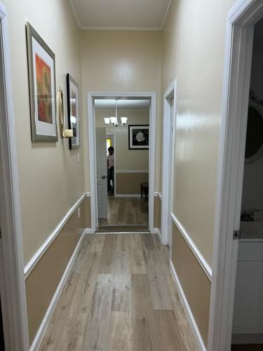 Narrow hallway with light-colored flooring and walls. Two doorways on the right and one on the left. Artwork hangs on the left wall.
