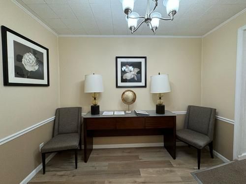 A waiting area with two chairs, a table with lamps, and framed floral art on the walls.