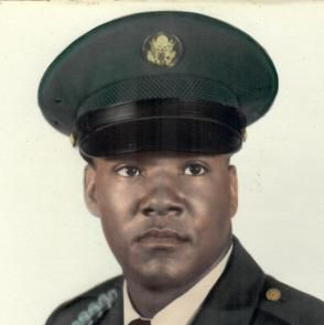 Man in military uniform, green hat with insignia, looking directly at the viewer.