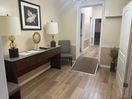 An entryway with light wood floors and beige walls. A ramp is in the hallway. A console table with lamps and artwork.