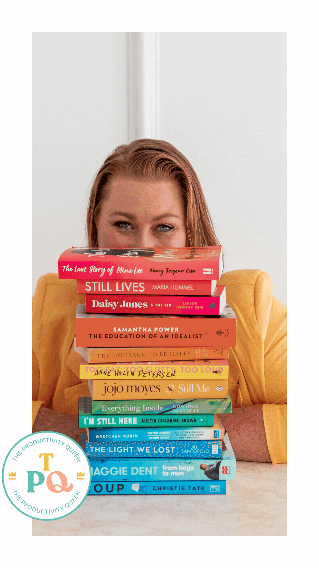 Woman peeking over a rainbow stack of books, wearing yellow blazer.