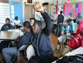 A boy in a classroom raising his hand to answer a question