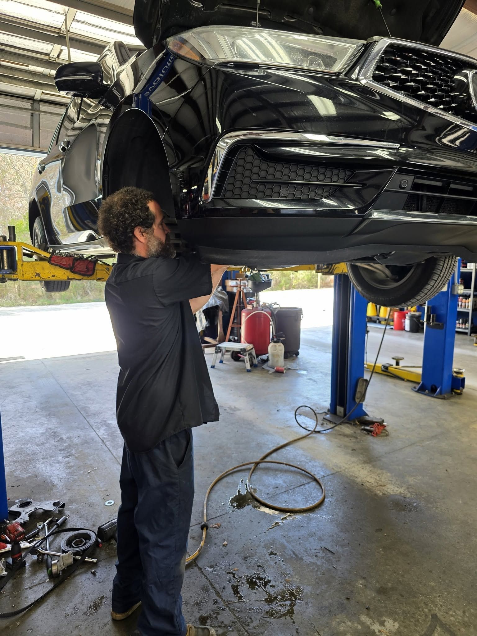 Mechanic working under a black car on a lift in an auto shop