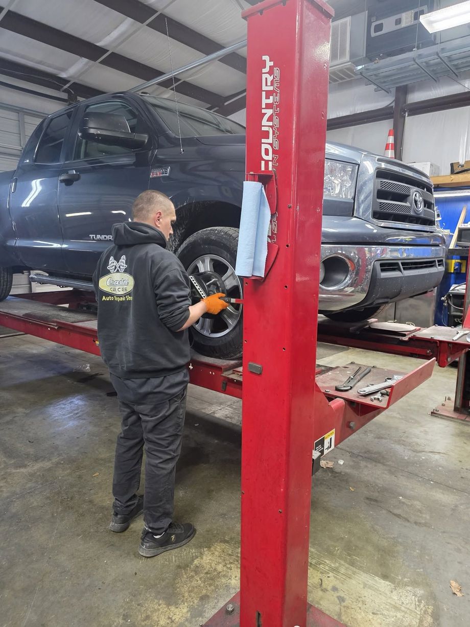 Mechanic working beside a blue SUV on a red car lift in an auto repair shop