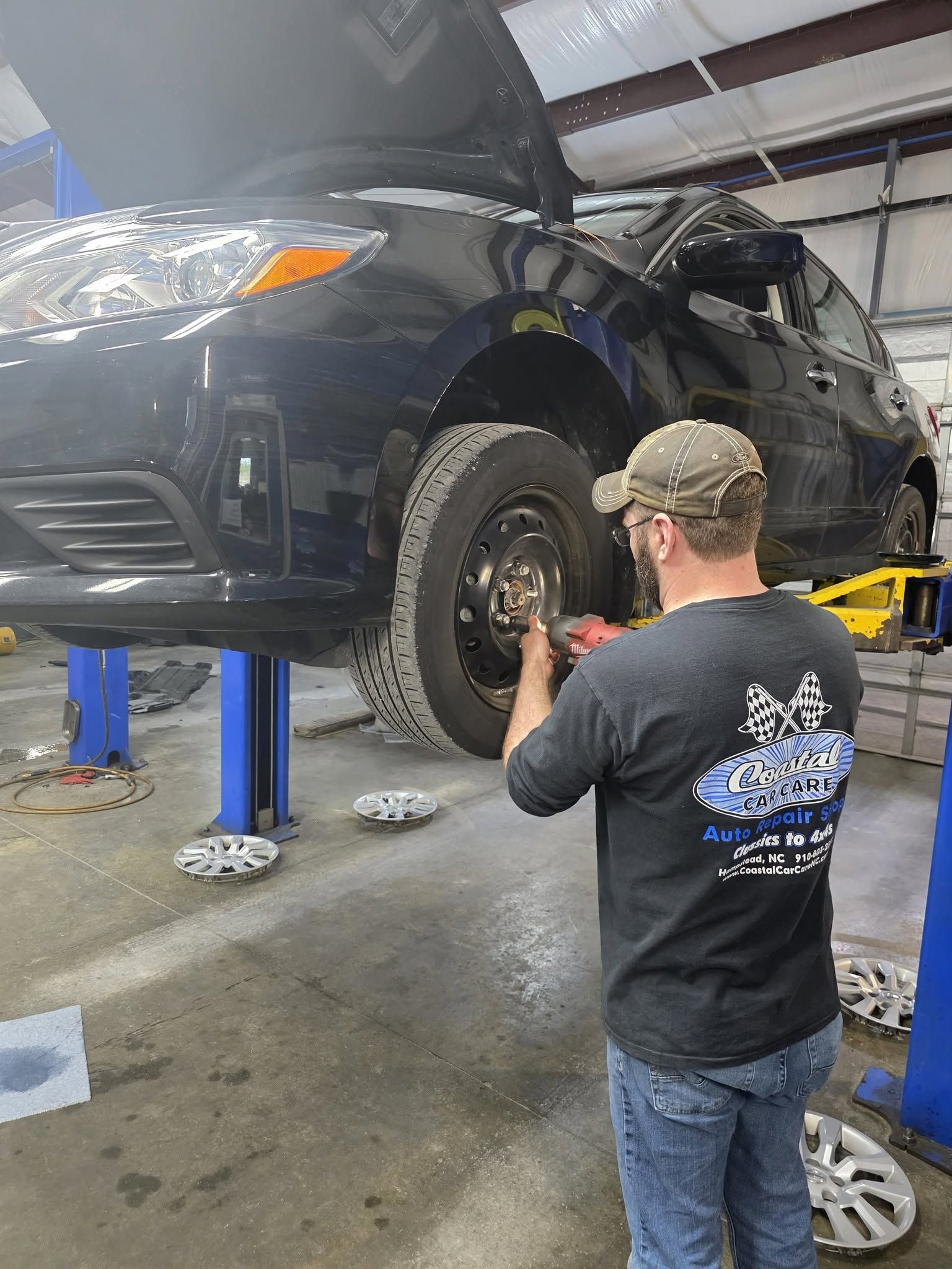 Mechanic inspecting a black SUV on a lift in an auto repair shop
