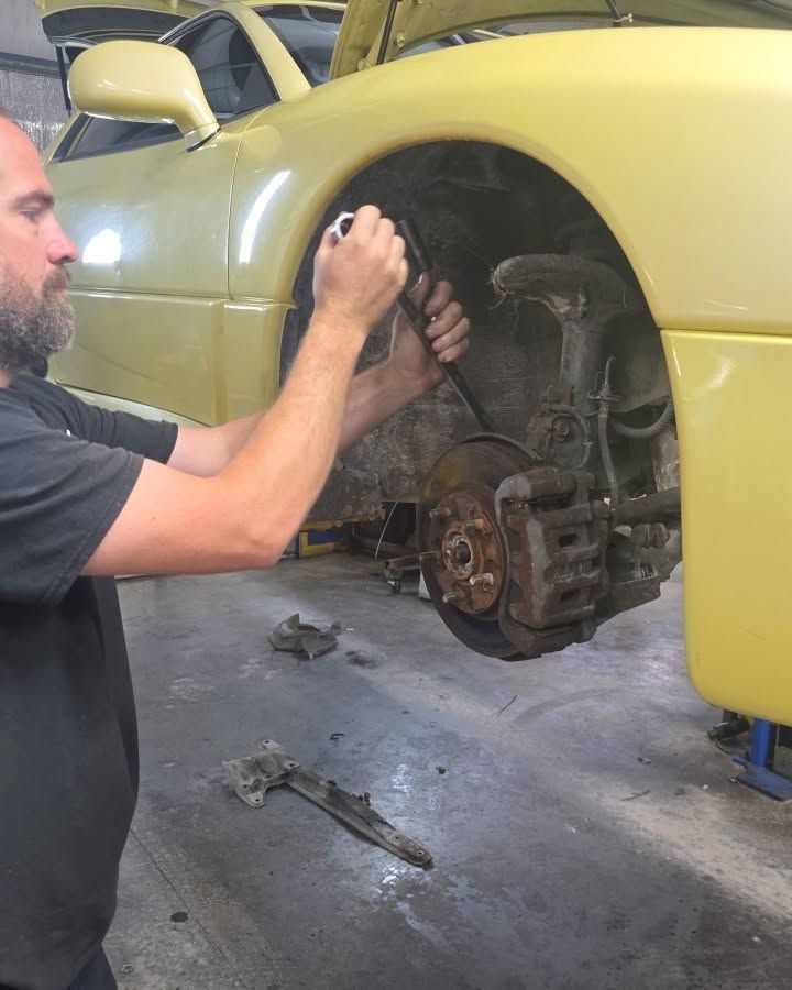 Mechanic working on a yellow car’s exposed front wheel assembly in a garage