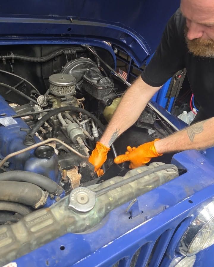 Mechanic in orange gloves working under the hood of a blue car engine
