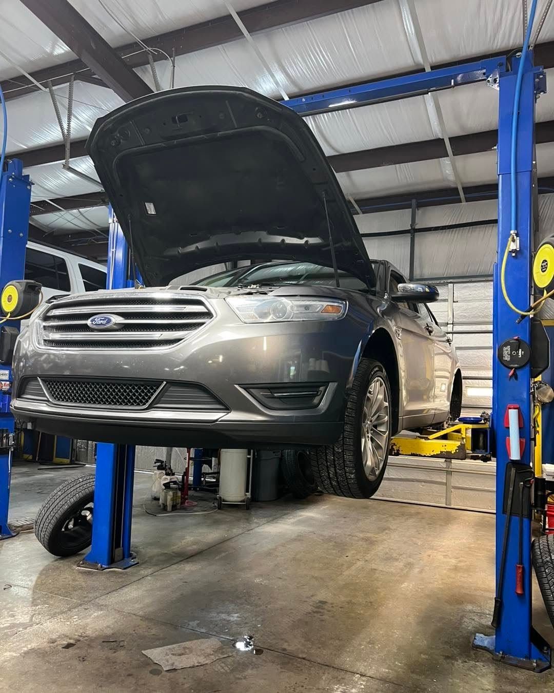 Silver SUV raised on a hydraulic lift in an auto repair shop with hood open