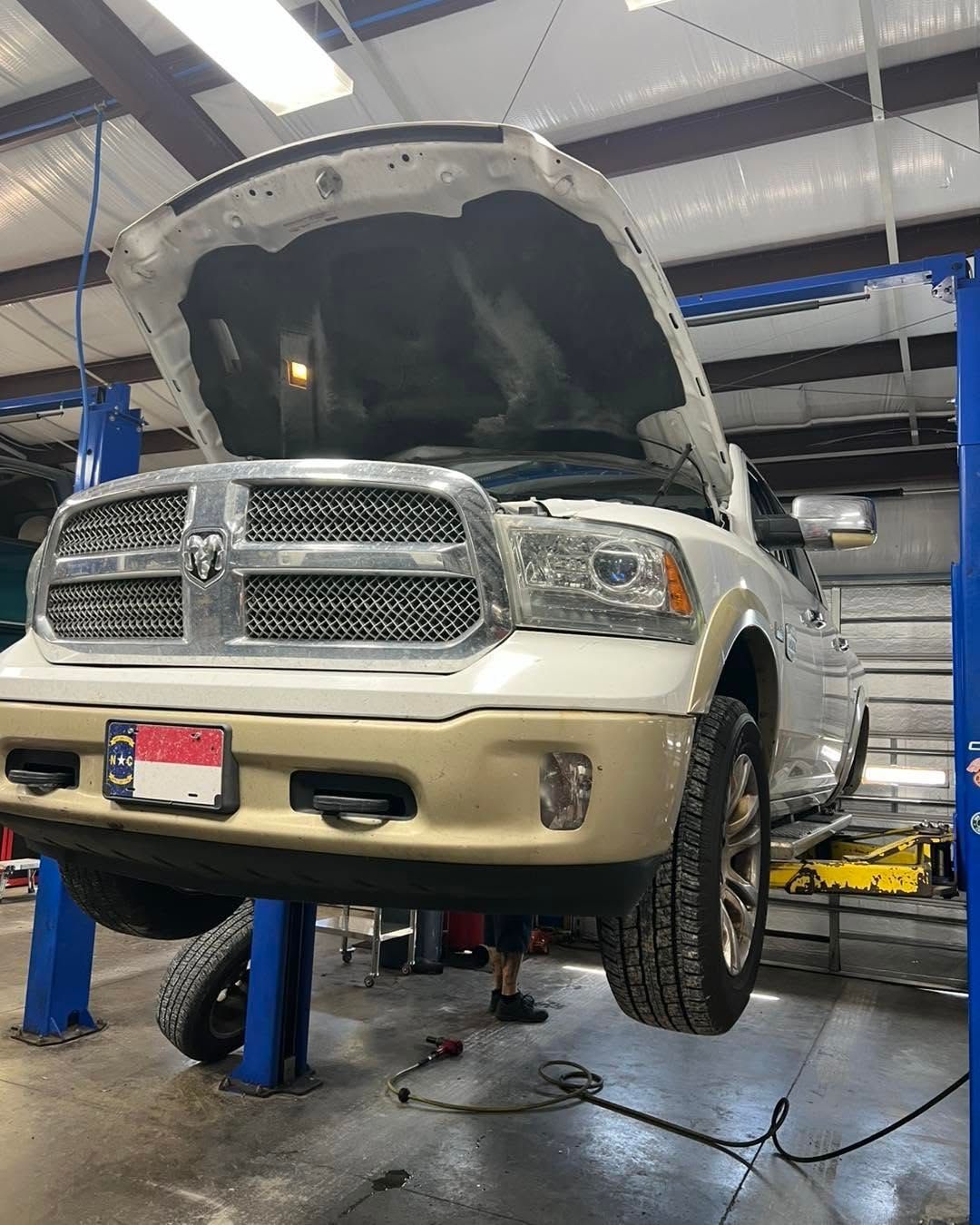 White pickup truck on a lift in an auto shop with hood open for repair