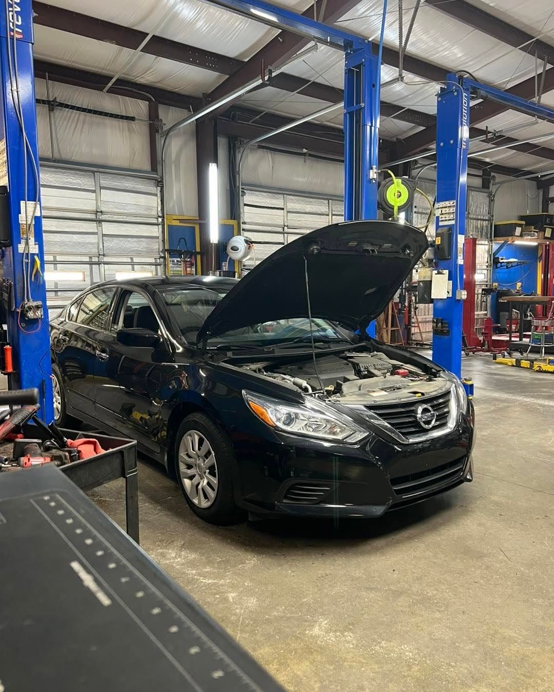 Black sedan with hood open in an auto repair shop between blue lifts