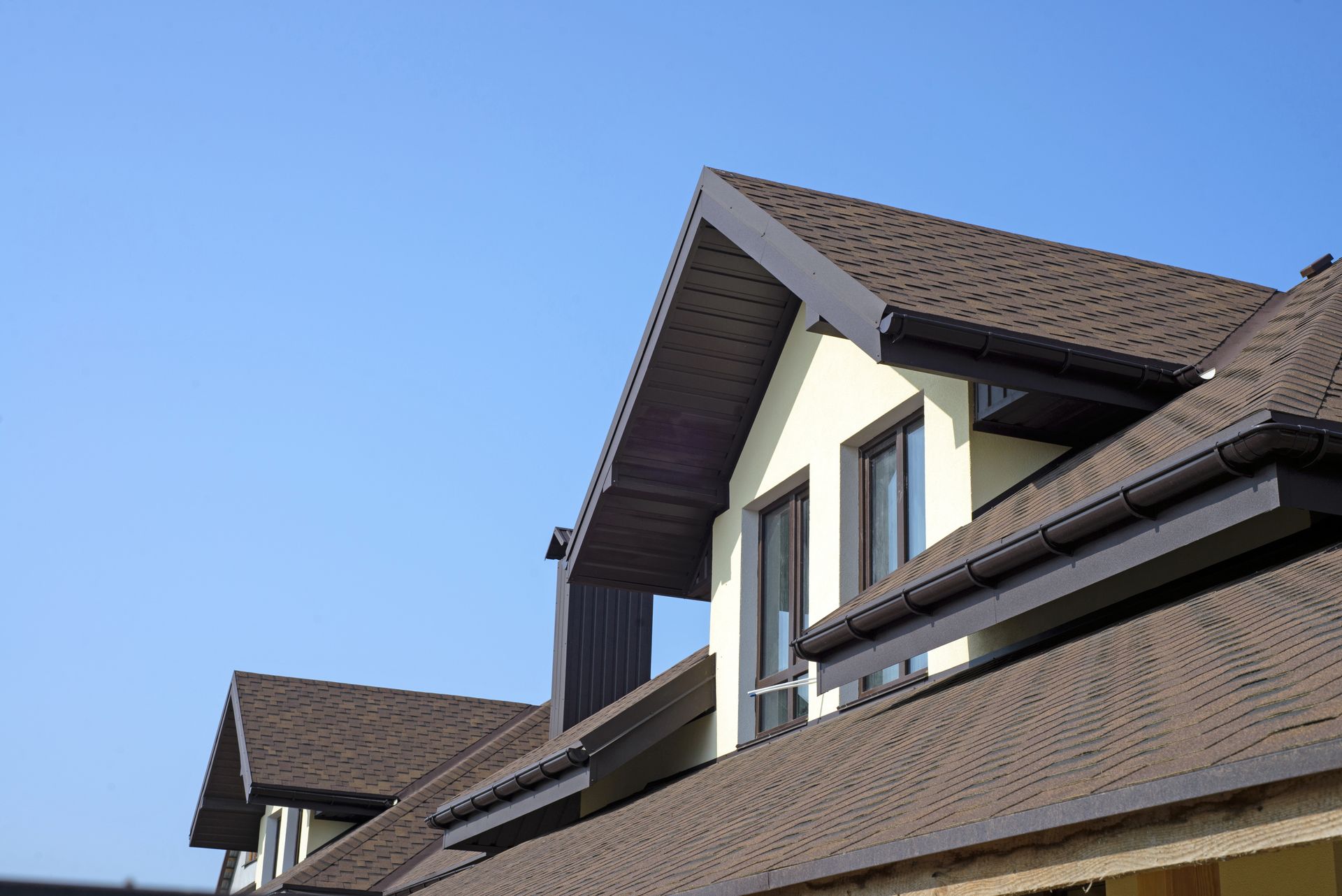 Modern house with pitched roofs and brown shingles against a clear blue sky.