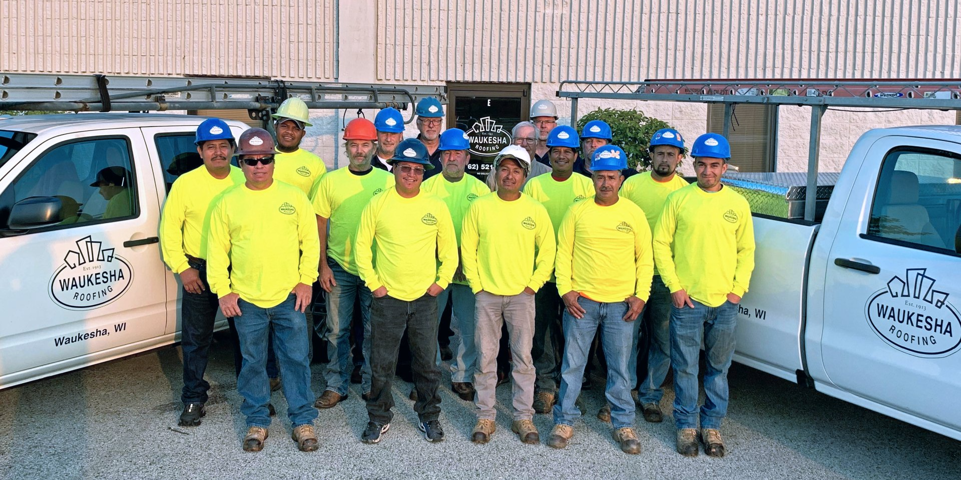 A group of construction workers are posing for a picture in front of their trucks.