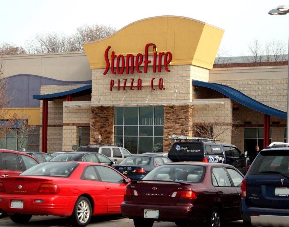 Cars are parked in front of a stonefire pizza co.
