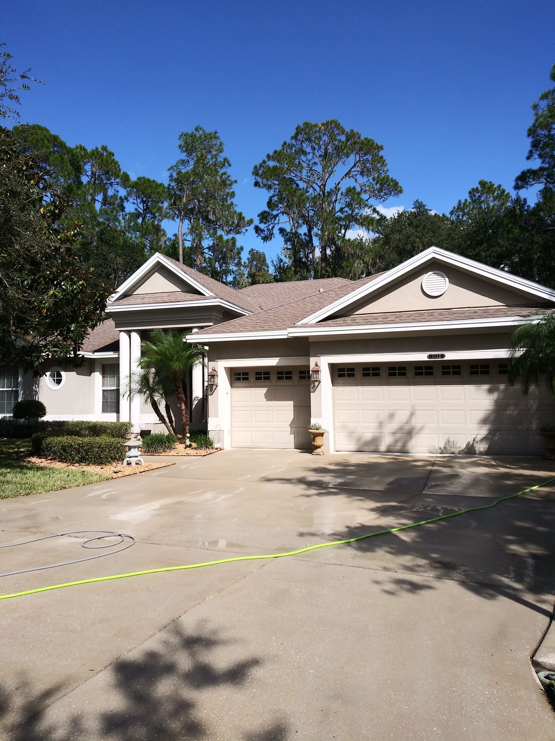 A house with two garage doors is surrounded by trees on a sunny day