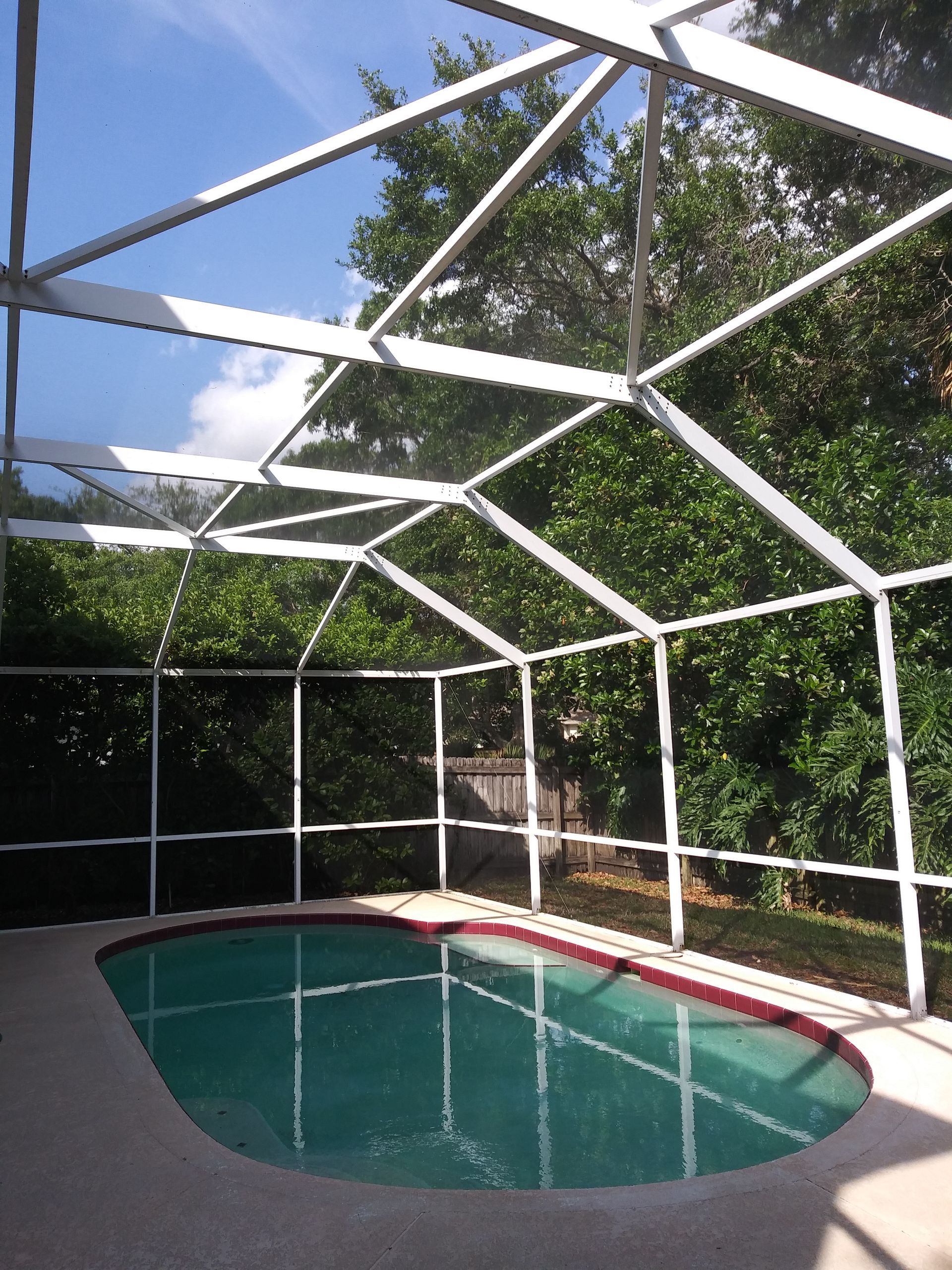 A screened in swimming pool with trees in the background