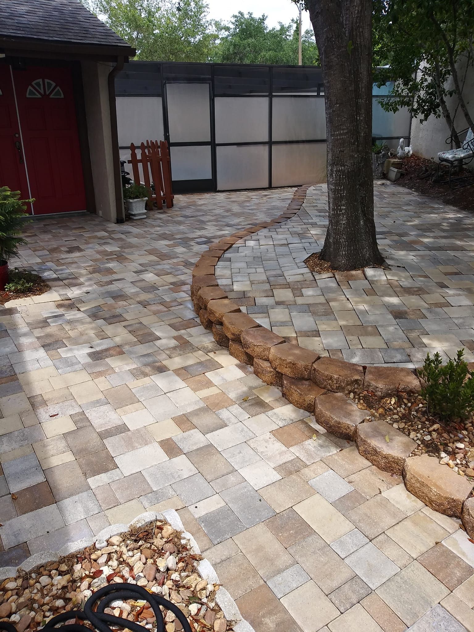 A brick walkway leading to a house with a tree in the middle